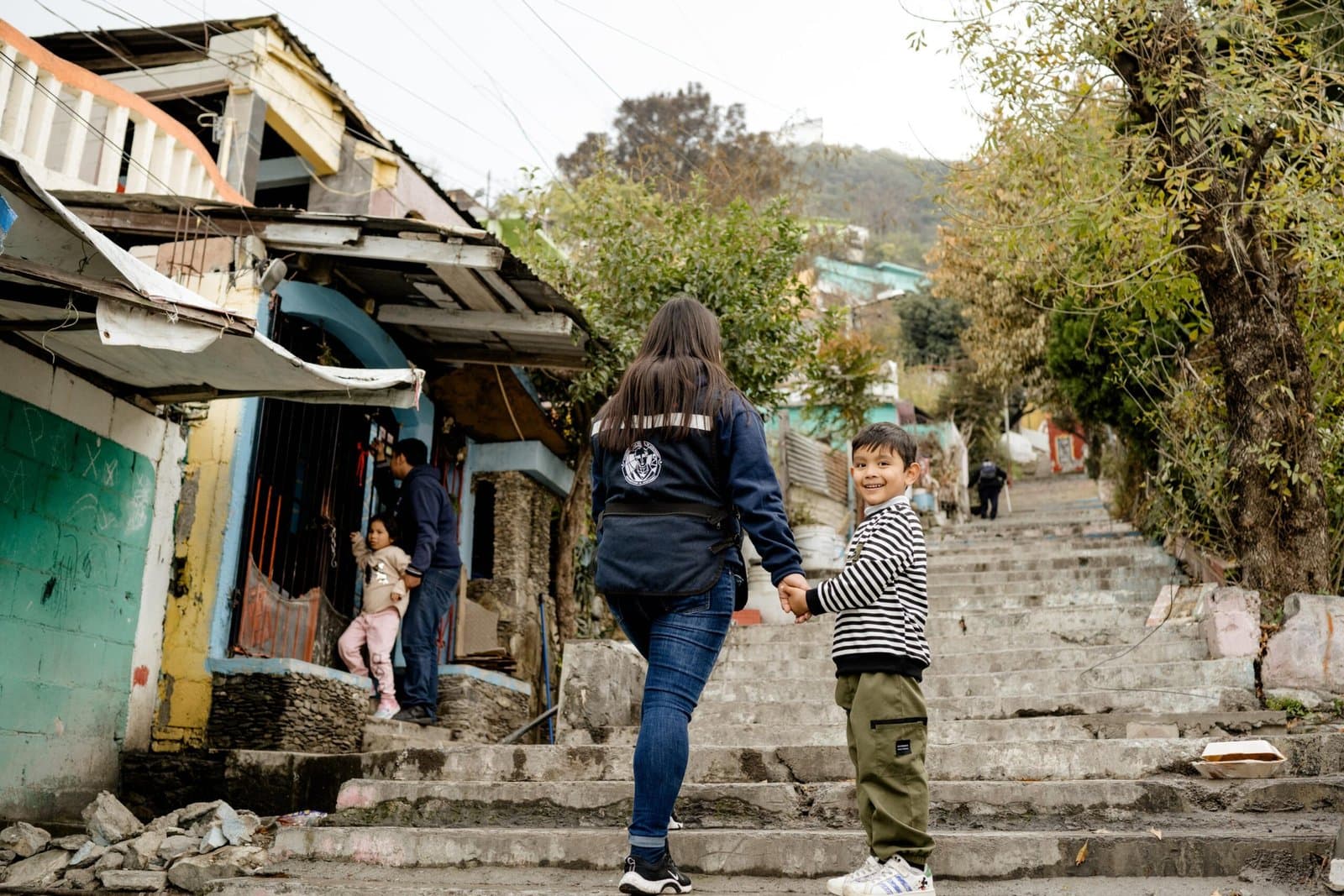 Una guía del Plan 20·40 sube las escaleras de la Colonia Independencia de la mano de un niño que voltea sonriendo